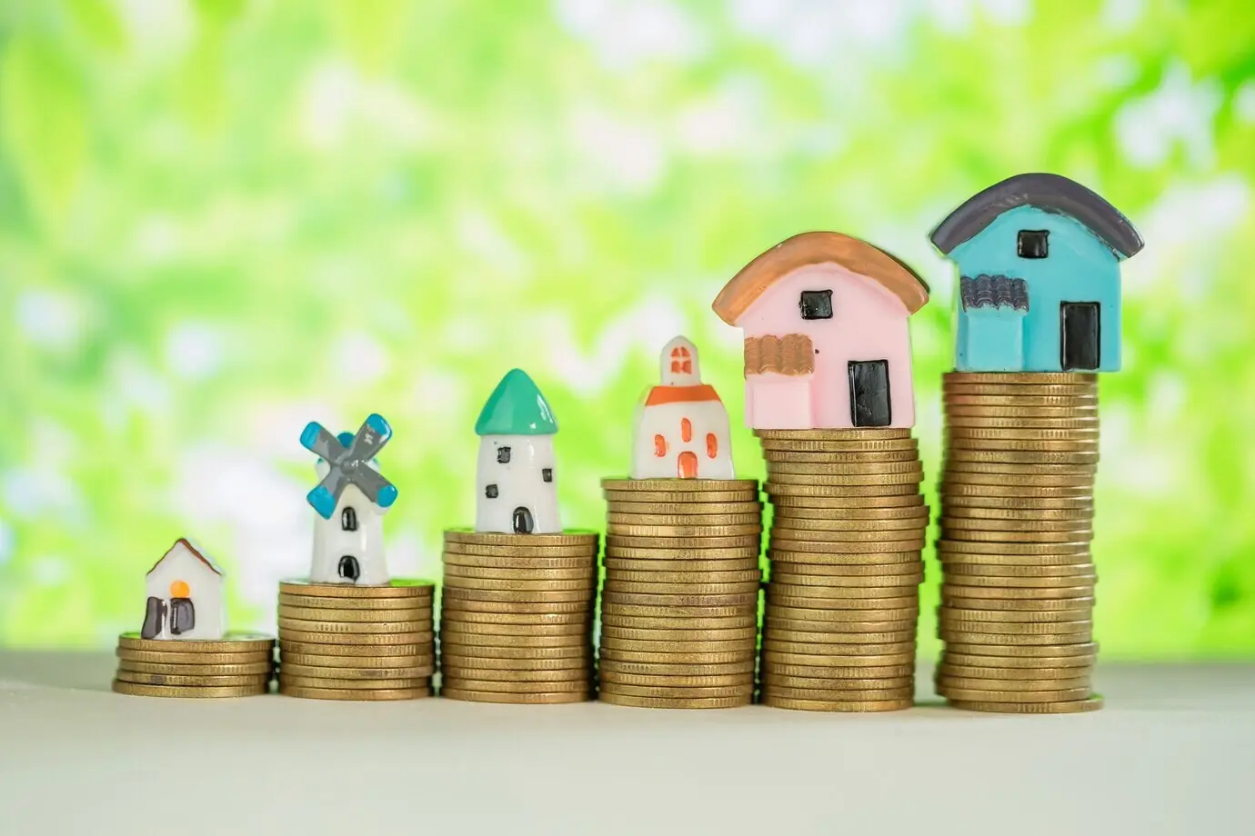 A miniature house on a stack of coins with a green blur.