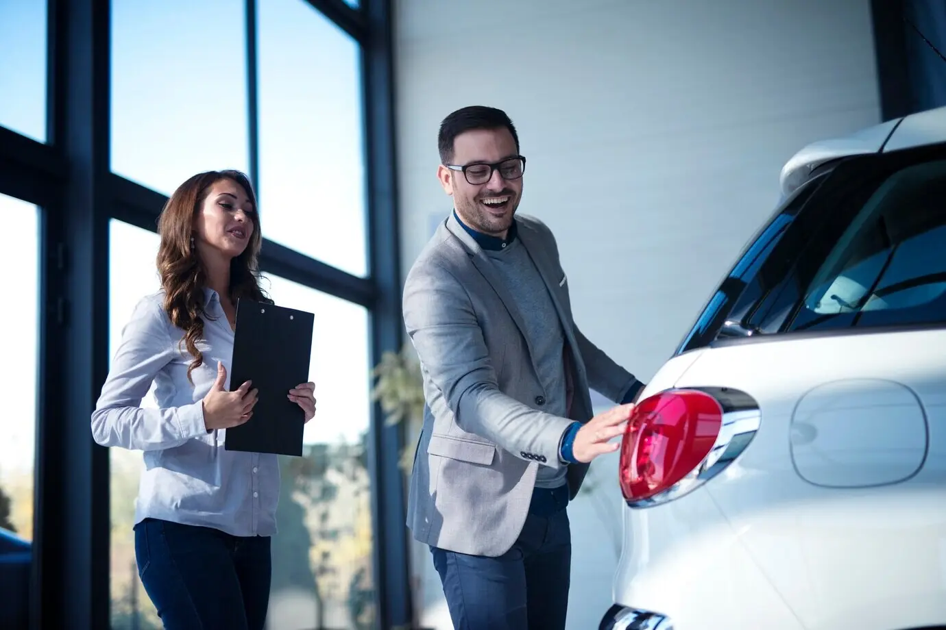 A well-dressed businessman is purchasing a new car while a salesperson presents the new vehicle to the customer.
