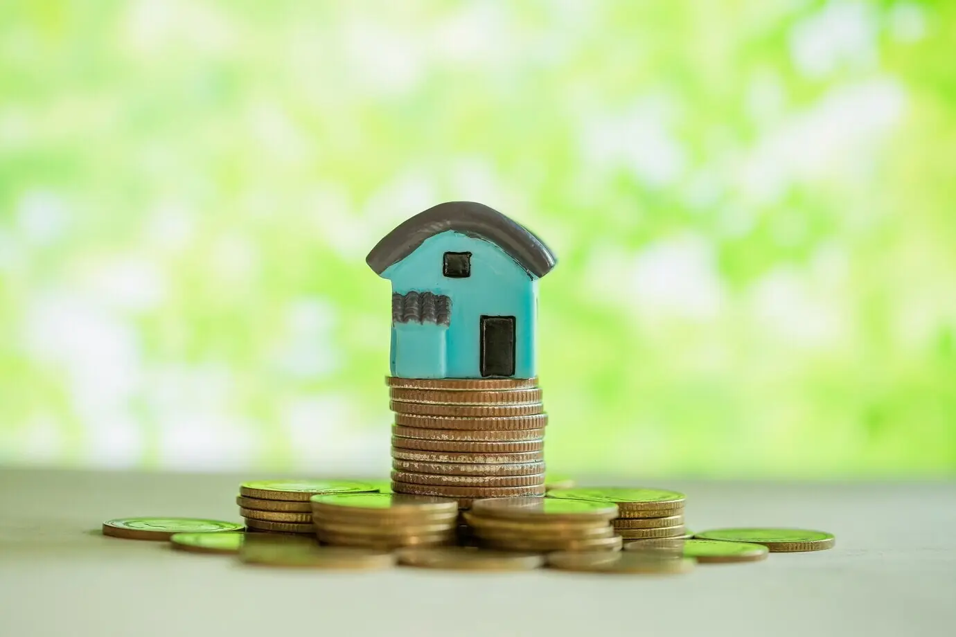 Miniature house on a stack of coins with green blur.